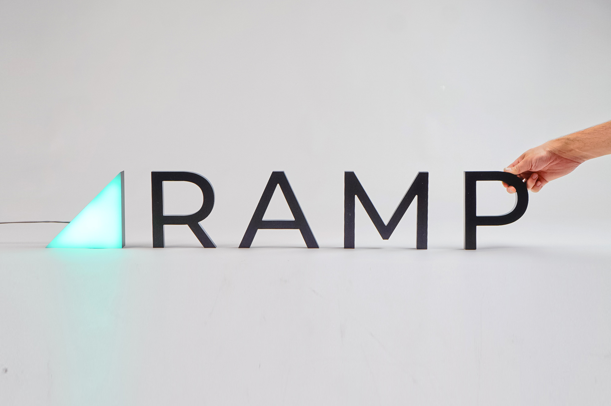 Illuminated, freestanding green triangle and black letters for Ramp, a technology company building the next generation corporate card to save businesses money.